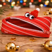 Red zipper pouch with a cartoon face on a wooden surface with festive decorations.