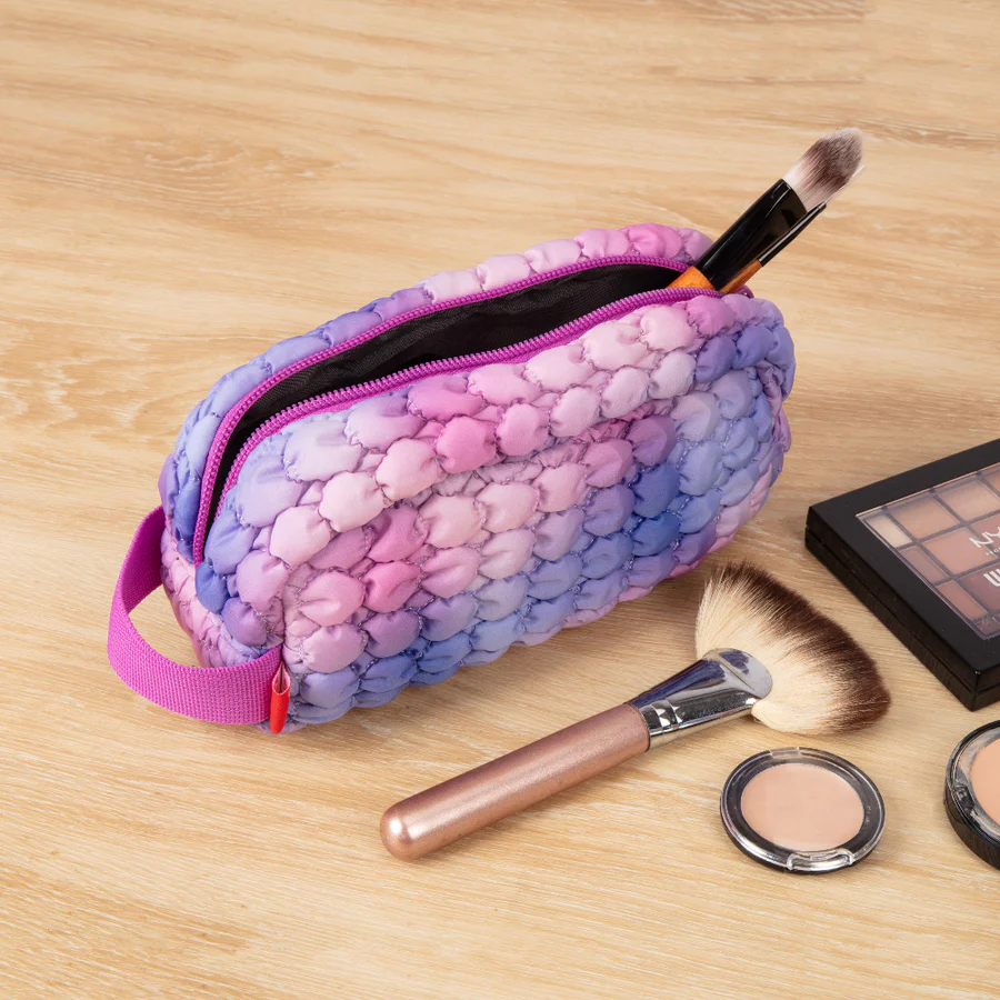 Makeup bag with makeup brushes and products on a wooden surface