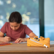 Dog-shaped pencil case on a table with a blurred child drawing in the background