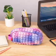 Colorful pencil case on a desk with laptop, tablet, and stationery items.
