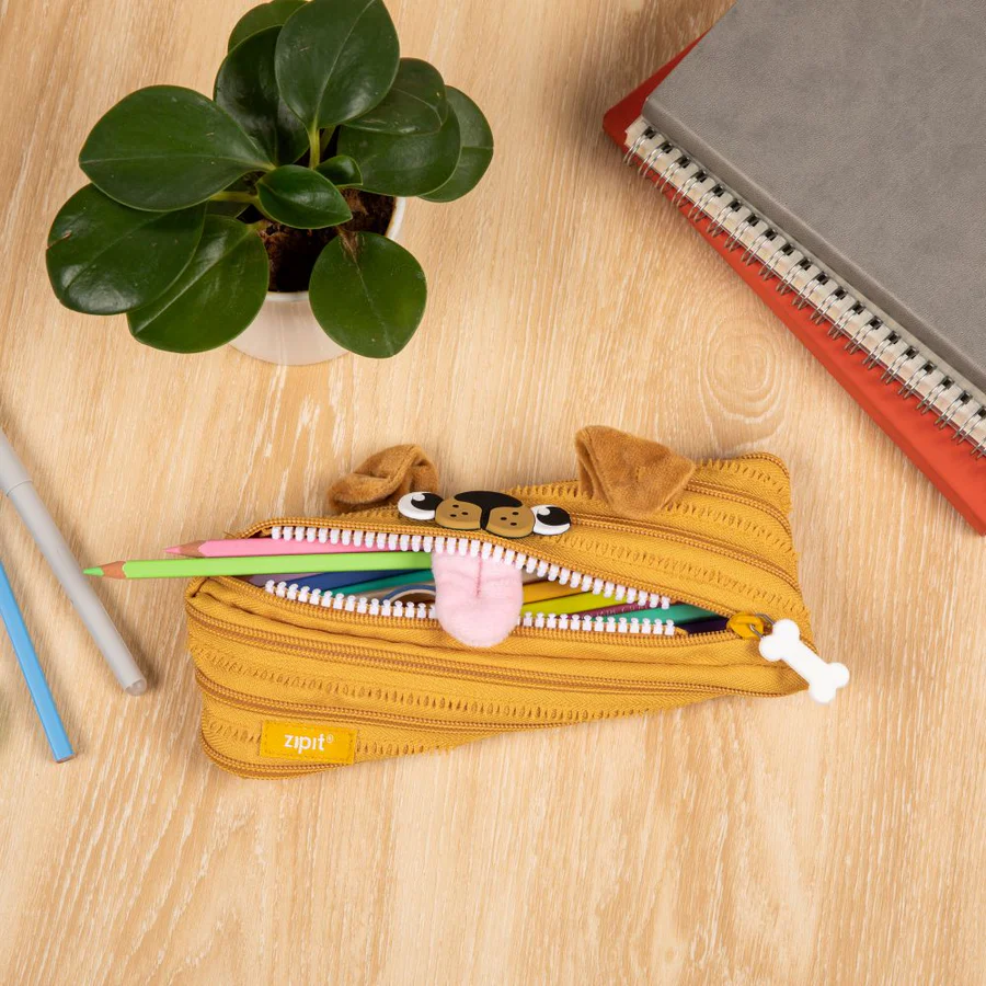 Yellow pencil case with cartoon face on a wooden surface with stationery items.